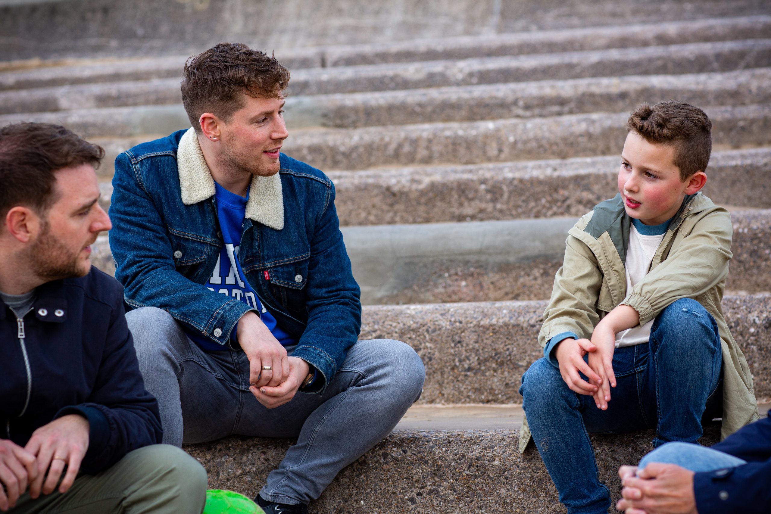 young boy and two males foster carers sat on steps